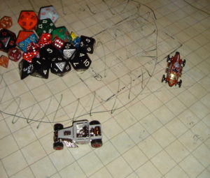 Matchbox cars -- small metal toys -- race on a grid map. A pile of dice appears in the upper-left corner.