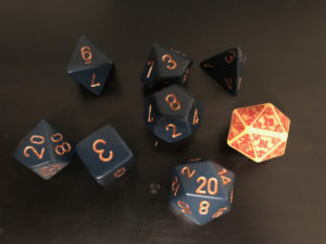 A set of dice for D&D. There are 7 blue dice with gold numbering, and one yellow die with red lettering.