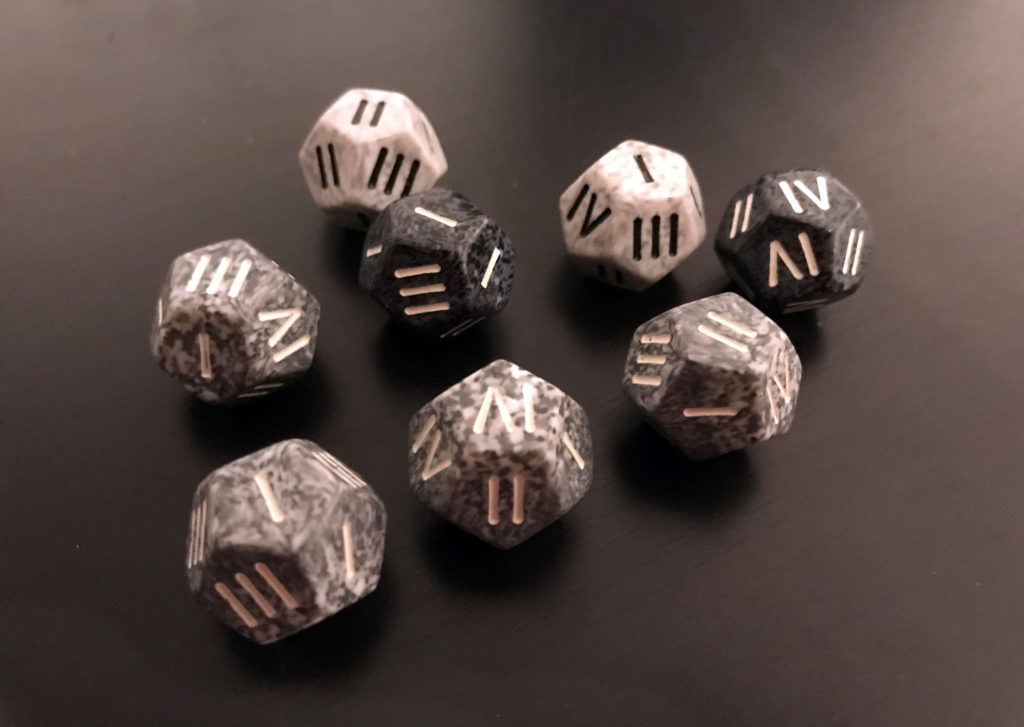 Different shades of grey twelve-sided dice, with the typical numbers replaced by Roman numerals.